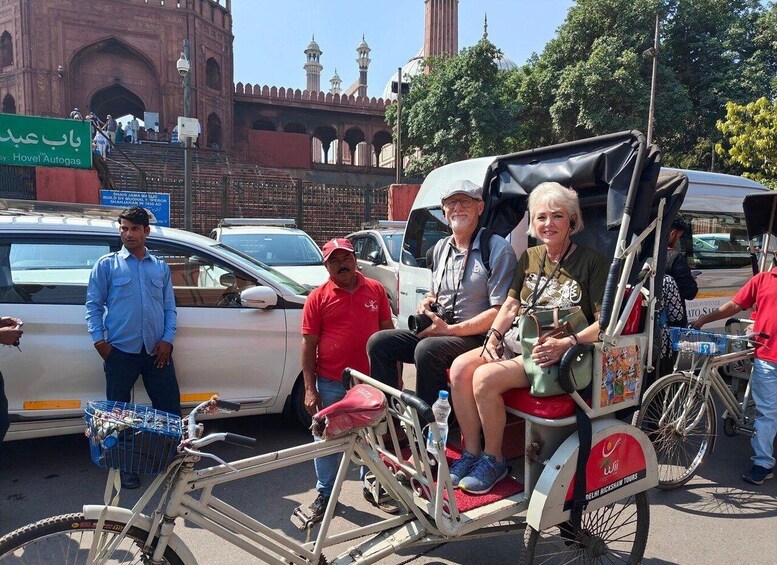 A rickshaw with passengers, a white car, and a historic building in the background. 3