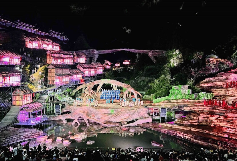 A nighttime outdoor theater with illuminated traditional buildings and a large rock formation stage. 2