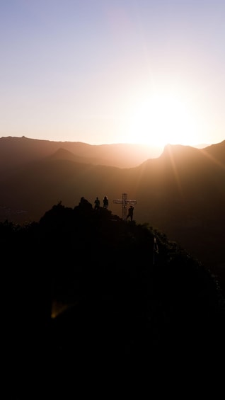A sunset over a mountain range with a cross structure silhouetted against the sky. 1