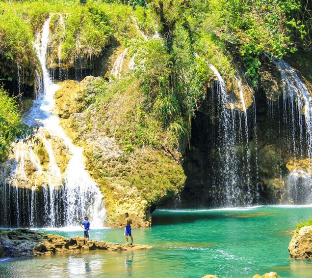 A waterfall cascading into a clear turquoise pool surrounded by lush greenery. 2