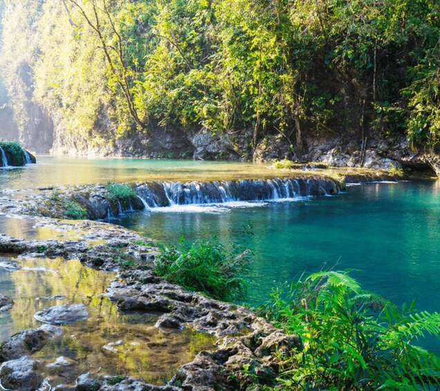 A serene river with clear water, a small waterfall, and lush greenery. 3