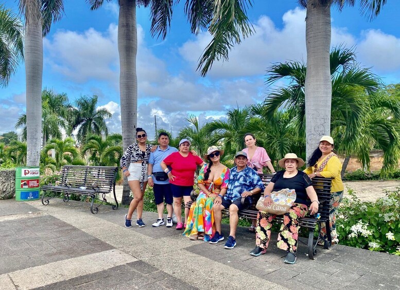 A group of people posing in a park with palm trees and a bench. 1