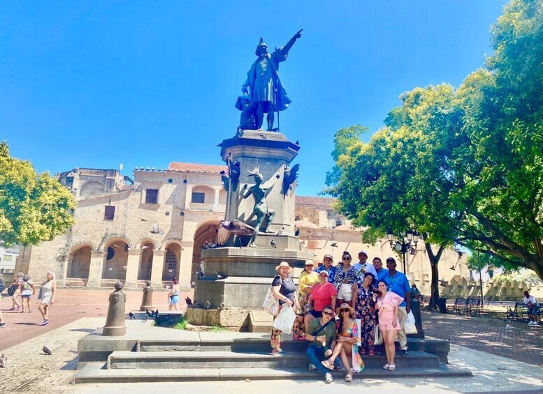 A group of people posing in front of a statue with a fountain, set against a historic building with arches. 4