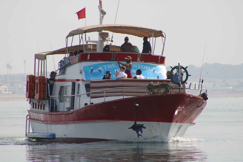 A red and white boat named 'The Intom' with people on board, sailing on calm waters. 4