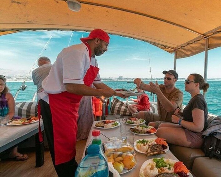 A group of people dining on a boat with a person serving food. 5