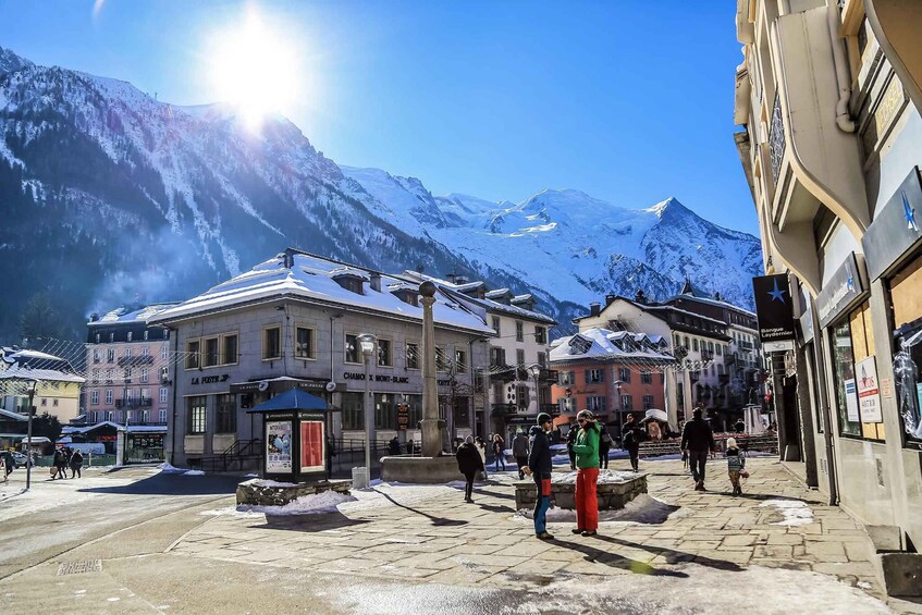 A snowy town square with buildings and mountains in the background. 1