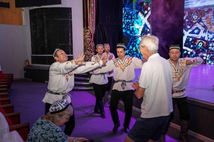 A group of people performing a dance on a stage with a large screen displaying abstract art in the background. 3