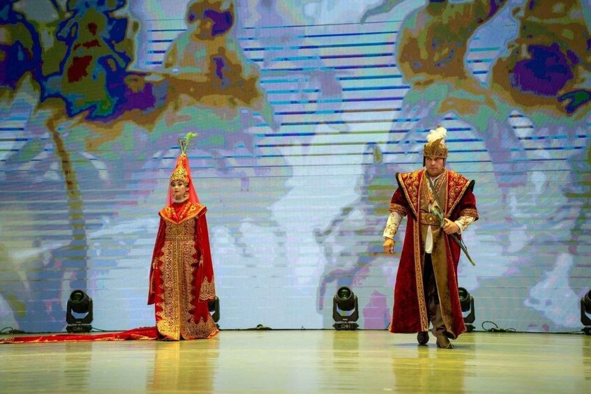 Two individuals in traditional costumes on a stage with a backdrop of a stylized landscape. 5