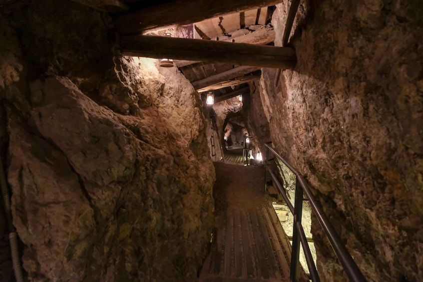 A narrow, dimly lit stone tunnel with wooden beams and metal railings. 4