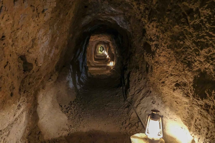 A narrow, dimly lit cave passage with a lantern on the right. 1