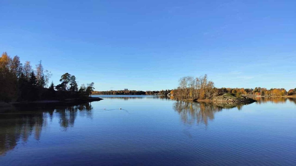 A calm lake with trees reflecting on the water, surrounded by a clear blue sky. 1