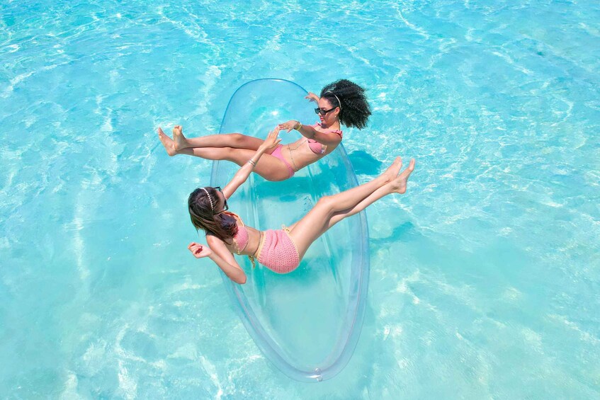 Two people floating on a clear blue inflatable tube in a swimming pool. 1
