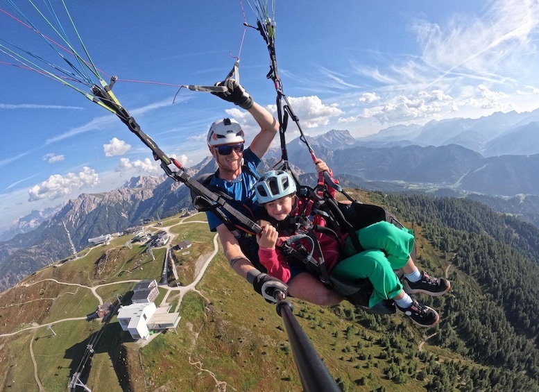Eine Person und ein Kind in einem Paragleitschirmsitz mit einer bergigen Landschaft im Hintergrund. 1