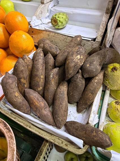 A market stall with sweet potatoes, oranges, and green fruits. 4