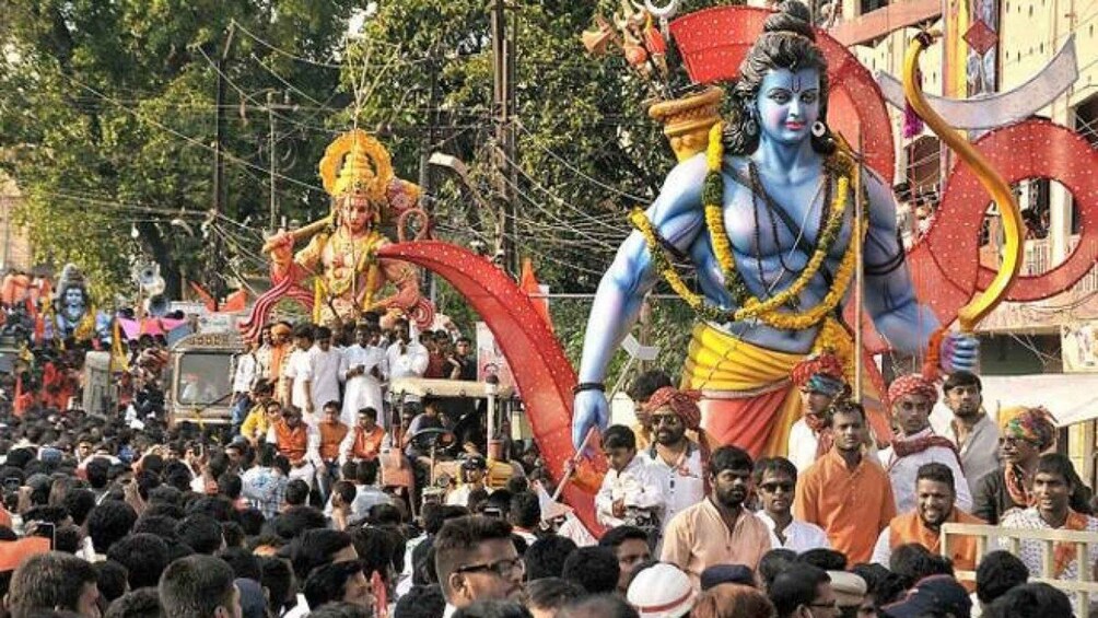 A religious procession with large statues of deities, a crowd of people, and a decorated float. 1