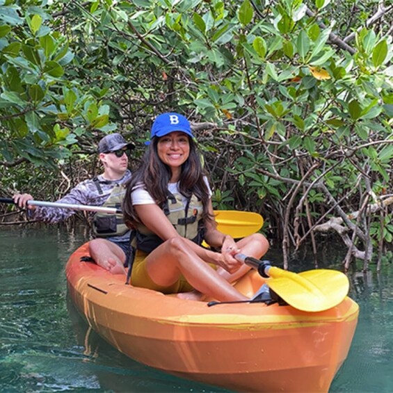 Two people in a small orange boat on a calm water body surrounded by dense mangrove vegetation. 5