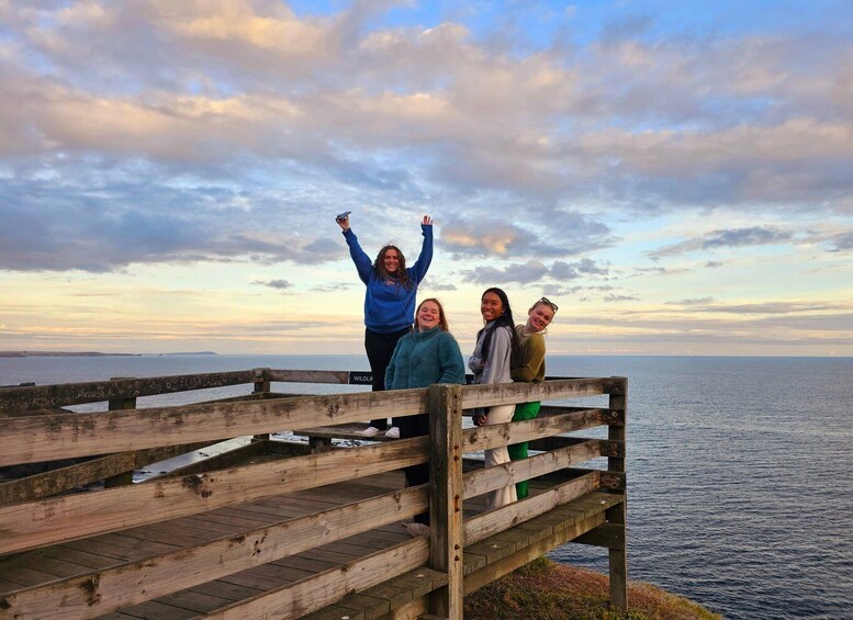 A group of people standing on a wooden pier with a view of the ocean and a cloudy sky. 4