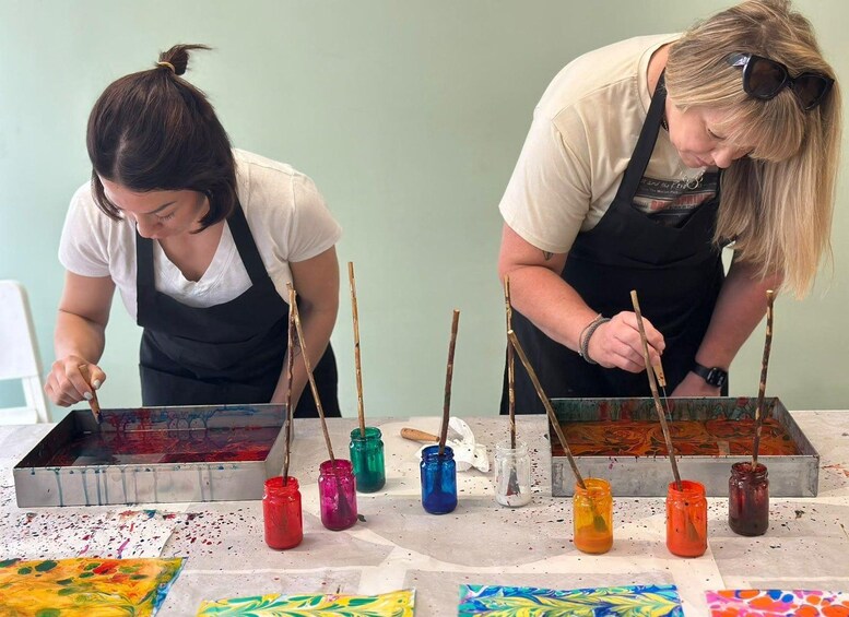 Two people painting with brushes dipped in various colors of paint on a table. 5
