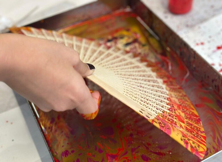 A hand holding a fan-like object over a colorful liquid surface. 2