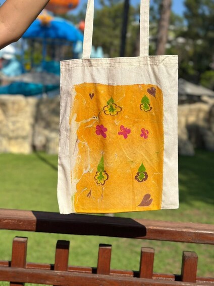 A hand holding a tote bag with a floral pattern, hanging from a wooden fence. 4