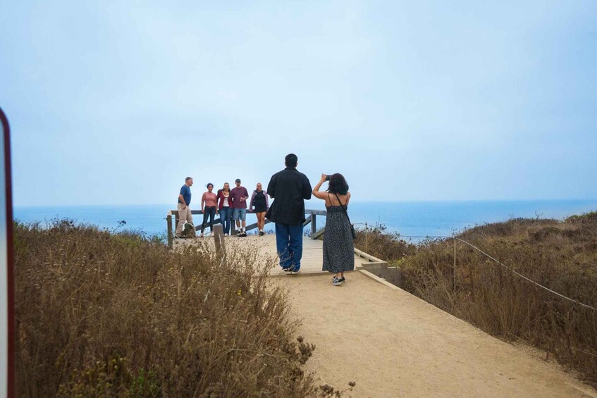 A group of people standing on a boardwalk by the sea. 2
