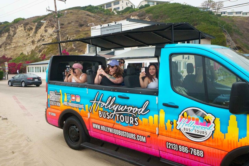 A colorful Hollywood Bus Tours vehicle with passengers taking photos. 5