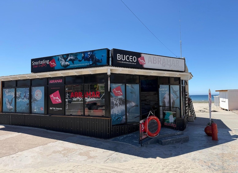 A beachside building with signage for 'ABRAMAR' and 'BUCEO', featuring large windows and a sandy ground. 2