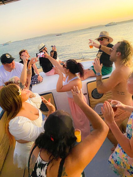 A group of people on a boat, some holding drinks, with a sunset in the background. 5