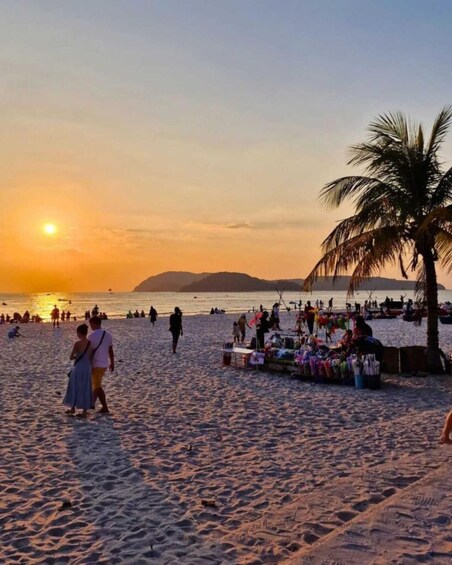 A beach at sunset with people walking and a market stall. 5