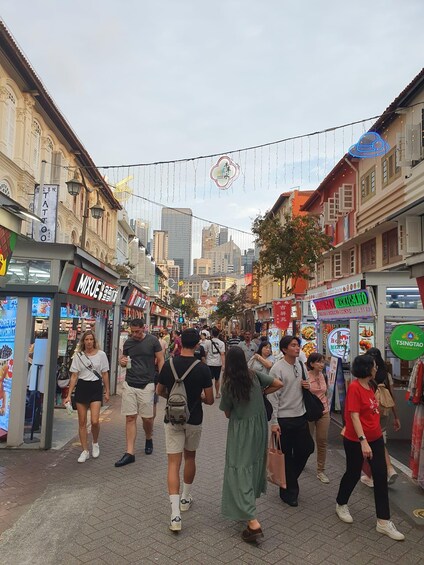 A busy street with people walking, shops, and hanging decorations. 2