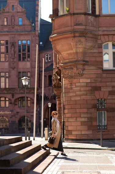 A woman descending a set of stone steps in front of a historic building with ornate architecture. 1