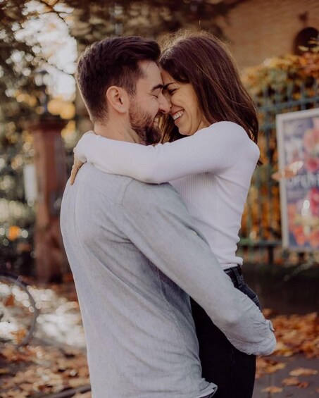 A couple embracing in an outdoor setting with trees and a building in the background. 2