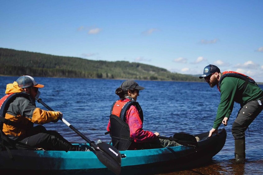 Three people in a canoe on a lake with a forested shoreline. 4