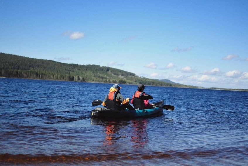 Two people kayaking on a calm lake with a forested shoreline. 1