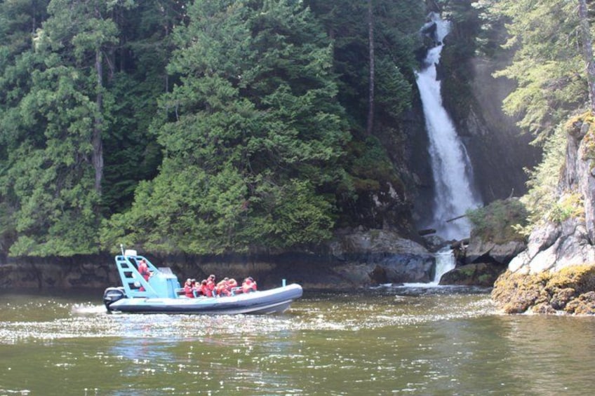A boat with passengers on a river, a waterfall, and dense forest in the background. 1