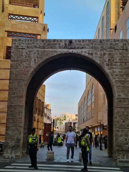 An archway in a city street with people walking and security personnel. 2