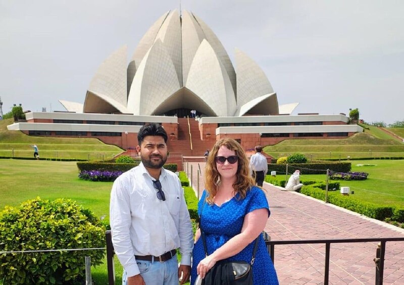 A couple standing in front of a large, white lotus-shaped building with a red base, surrounded by well-manicured lawns and pathways. 2