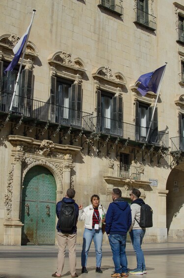 A group of people standing in front of a historic building with ornate architecture and flags. 4