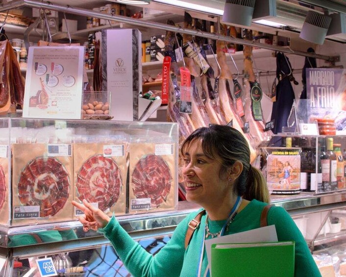 A person pointing at a display of cured meats in a store. 5
