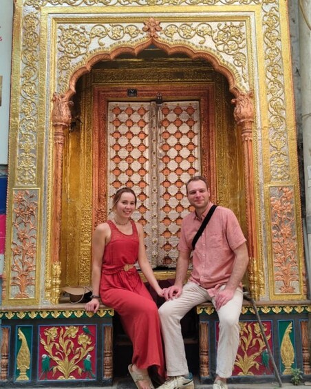 A couple sitting in front of a richly decorated doorway with intricate patterns and gold accents. 5