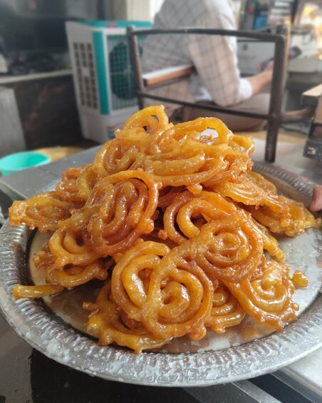 A plate of jalebi, a popular sweet treat, in a busy setting. 2