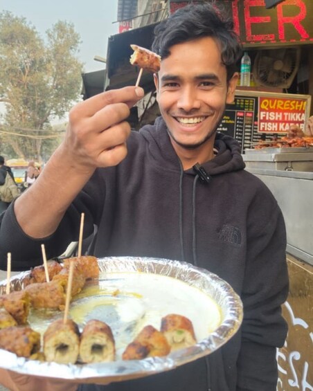 A person holding a plate with food items, including skewered pieces and a white sauce. 4