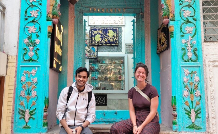 Two people sitting on a bench outside a shop with turquoise walls and floral decorations. 3