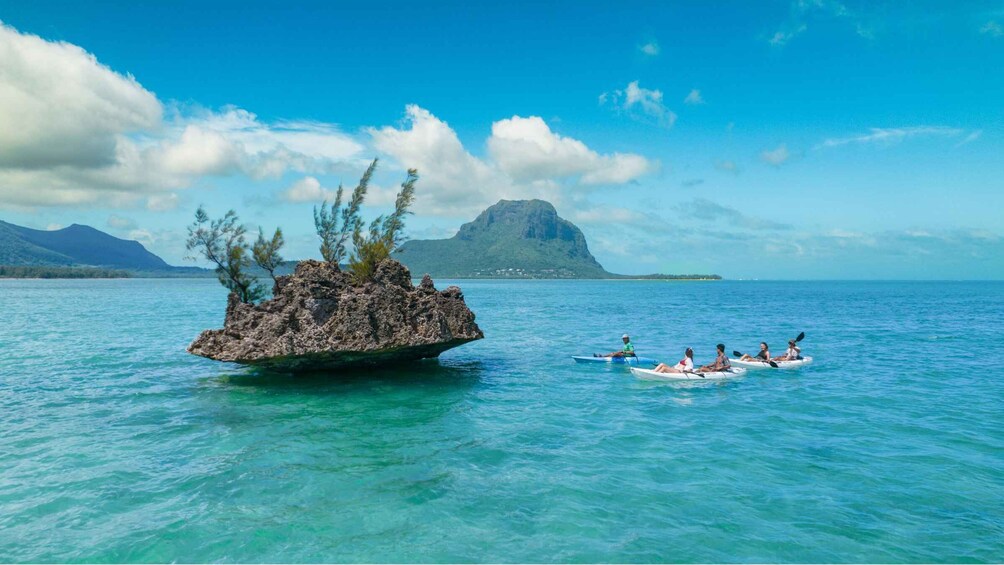 A clear blue sea with a small rocky island and kayakers in the foreground. 1