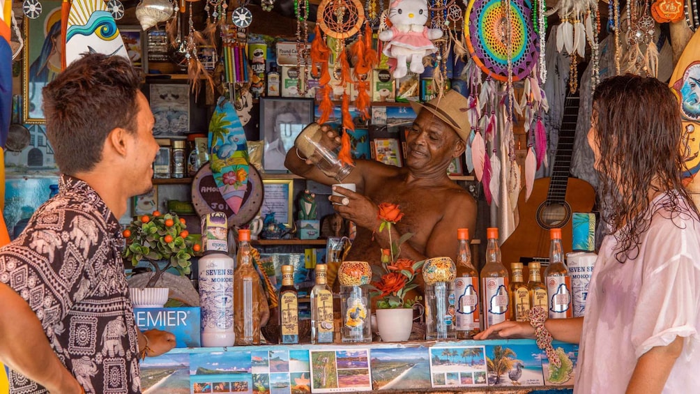 A person pouring a drink at a counter with various bottles and decorative items. 3