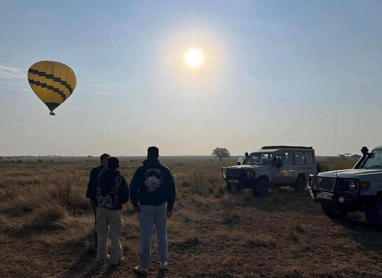 A hot air balloon, two people, and a safari vehicle in a grassy field. 3