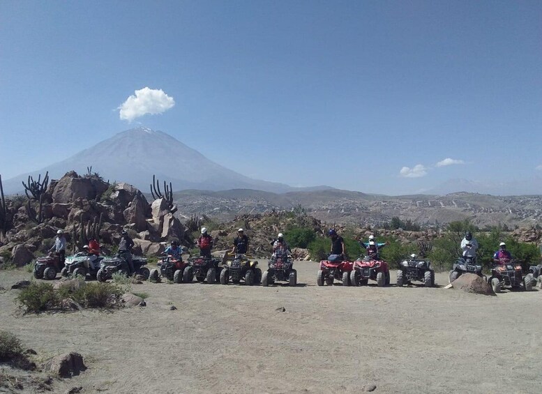 Un groupe de personnes à bord de quads dans un paysage désertique, avec un volcan en arrière-plan. 3