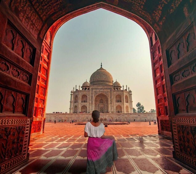A person sitting in an ornate doorway with the Taj Mahal in the background. 1