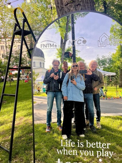 A group of people standing in front of a mirror reflecting a building and trees. 2