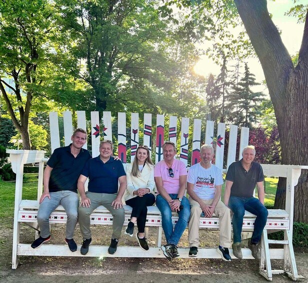 A group of people seated on a white wooden bench with colorful decorations in a park. 1